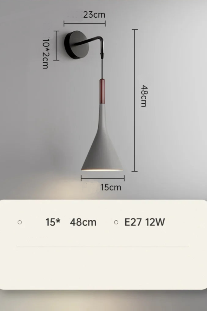 A modern silver wall lamp mounted on a wall with a switch, next to a grey headboard and a window with blue curtains.