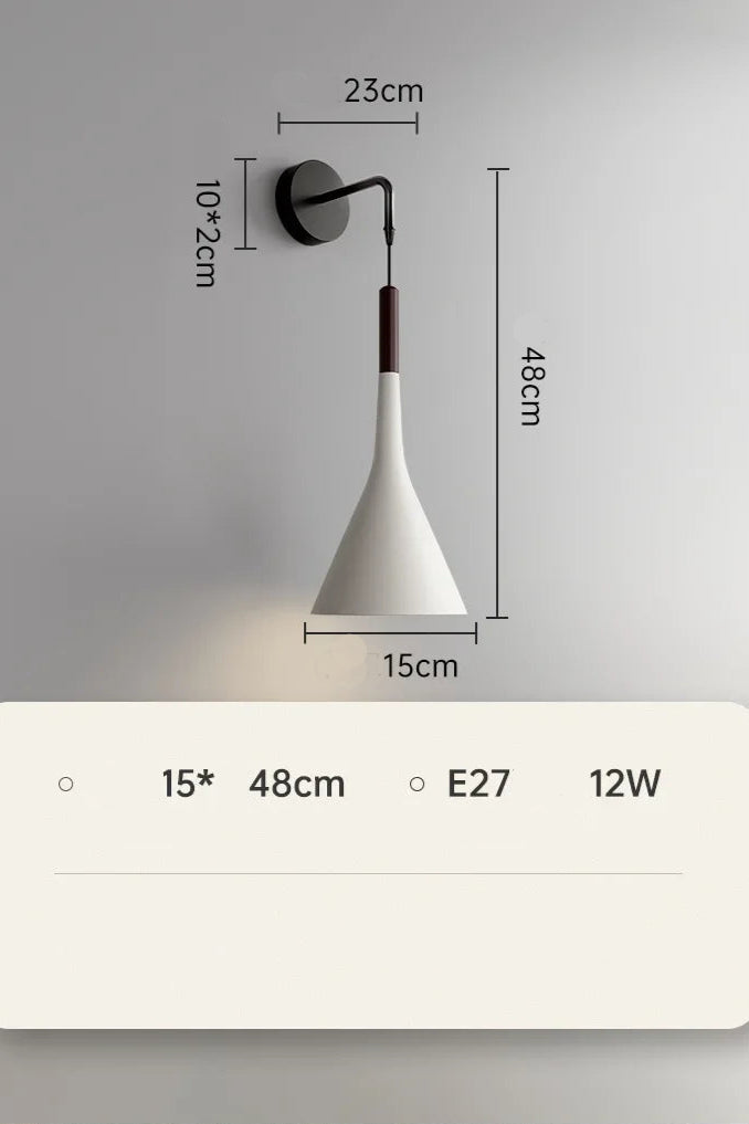 A modern silver wall lamp mounted on a wall with a switch, next to a grey headboard and a window with blue curtains.