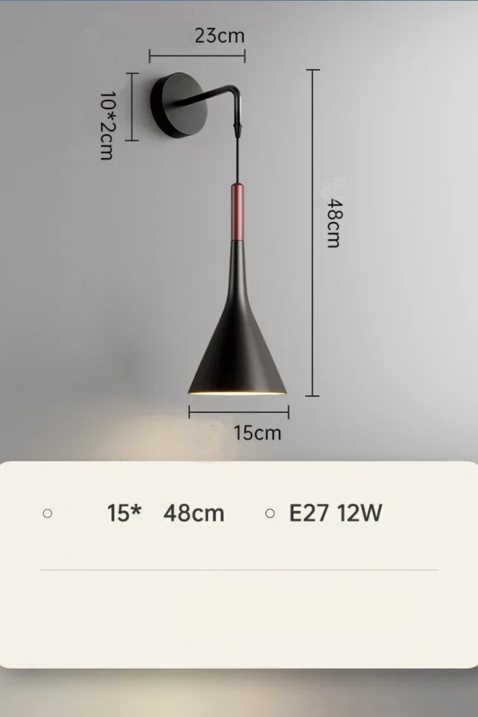 A modern silver wall lamp mounted on a wall with a switch, next to a grey headboard and a window with blue curtains.